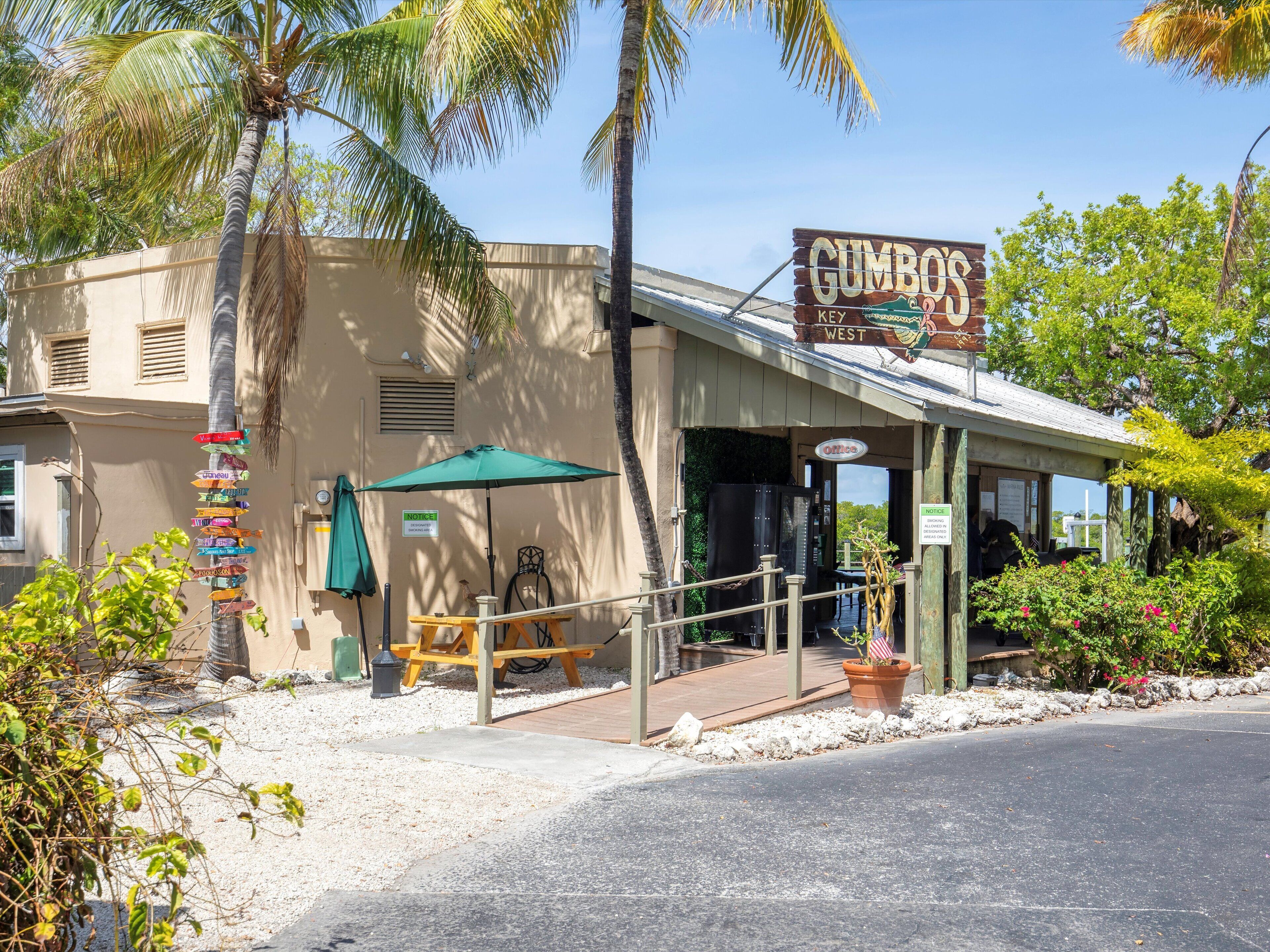 Edifici amb un rètol que diu "Gumbo's Key West" i una zona de pati amb una taula, caires i un parasol.
