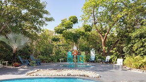 A pool area with a clear blue pool, surrounded by trees and outdoor seating. - Poolside Cottage #412 (Key West)