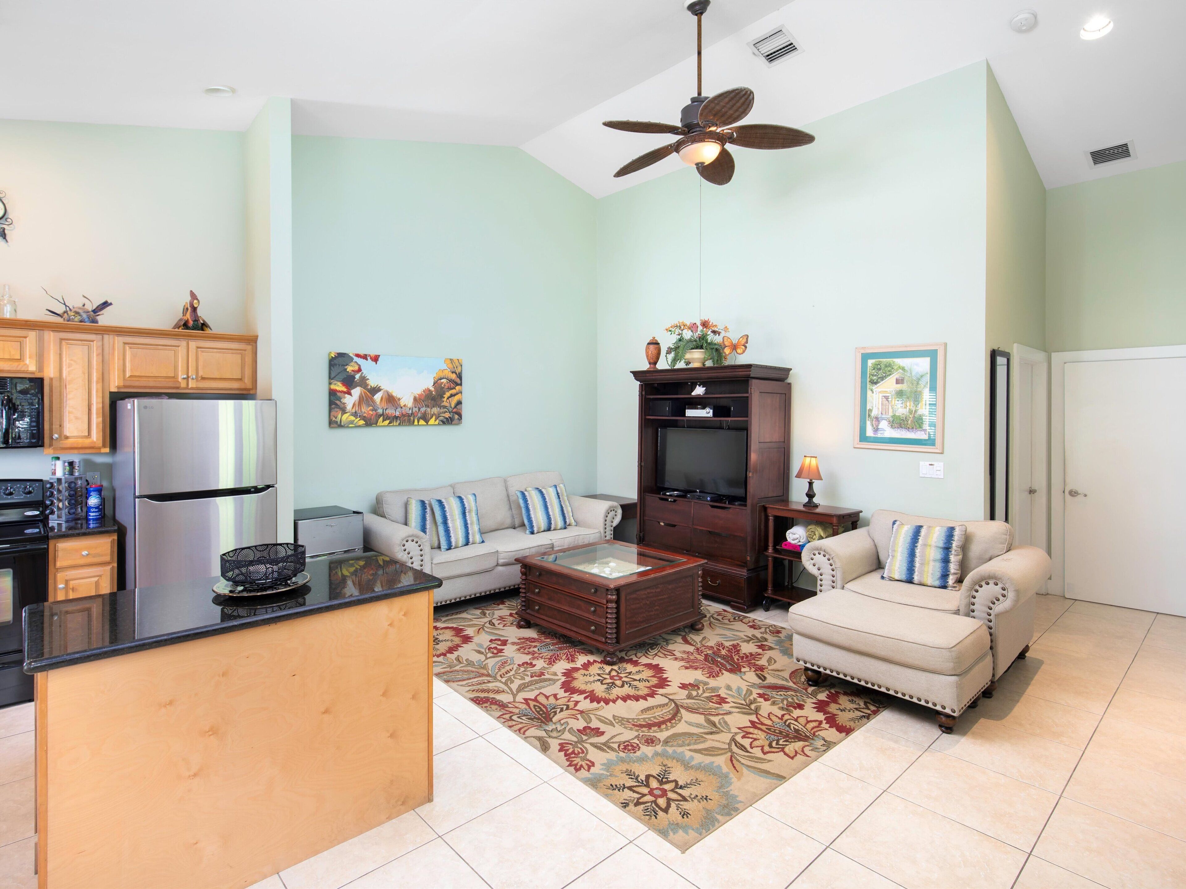 A living room with a sofa, coffee table, TV stand, and kitchen area with appliances.