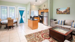A spacious living room with a sofa, a coffee table, and a dining area with wicker chairs. - Poolside Cottage #412 (Key West)