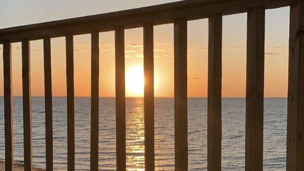 A wooden deck with a railing overlooking a beach at sunset.
