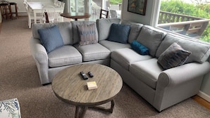 A living room with a grey sectional sofa, a round wooden coffee table, and a dining area with a white table and chairs.