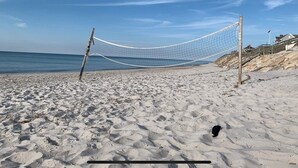 A beach volleyball net set up on a sandy beach with a clear sky and ocean in the background.
