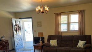 A living room with a brown sofa, patterned rug, wooden coffee table, and a chandelier. - Harbor House (Chincoteague)