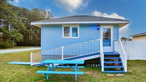 A small, single-story house with a blue exterior, a front porch with a white railing, and a set of stairs leading to the front door. - Harbor House (Chincoteague)