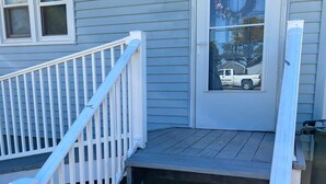 A wooden staircase leading to a front door with a wreath, a window with a view of a truck, and a white railing. - Harbor House (Chincoteague)