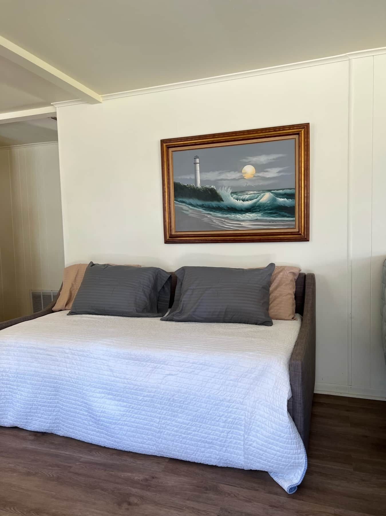 Un dormitorio con cama, almohadas y un cuadro de un faro en la pared.