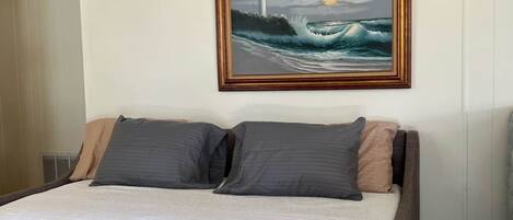 Un dormitorio con cama, almohadas y un cuadro de un faro en la pared.