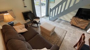 Una sala de estar con un sofá marrón, un sillón mecedora, un televisor y una escalera.