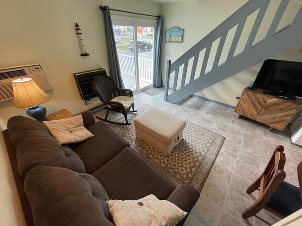A living room with a brown sofa, a rocking chair, a television, and a staircase. - Surfers Villa (Chincoteague)