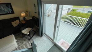 Habitación con sofá, una silla, una lámpara y puerta corrediza de vidrio que da a una terraza al aire libre.
