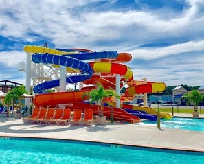 A water park with multiple water slides in blue, red, and yellow, a pool, and lounge chairs. - Surfers Villa (Chincoteague)
