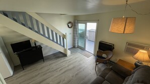 A spacious living area with a staircase leading to a balcony, a sofa, a television, and a lamp.