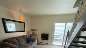 A spacious living room with a grey sofa, a wooden dining table, and a staircase leading to an upper level. - Sand Dollar Villa (Chincoteague)