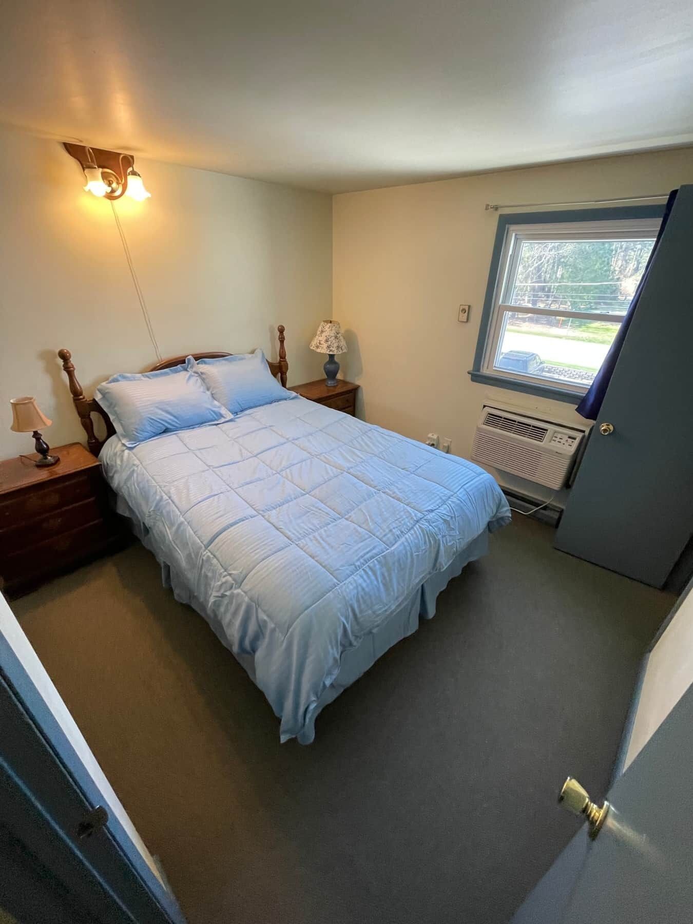Een slaapkamer met een bed, nachtkastjes, een lamp, een raam en een radiator.