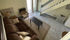 Una sala de estar con un sofá marrón, una mesita y una silla. Se ve una escalera que sube a un nivel superior.