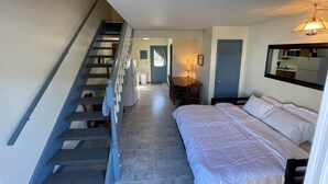 A bedroom with a bed, a desk, and a chair. There is a staircase leading to another room.