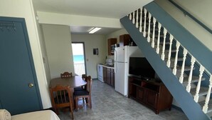 A compact living space with a kitchenette, a dining area, and a staircase. - Flamingo Villa (Chincoteague)