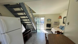 A compact kitchen with a refrigerator, a wooden dining table, and a staircase leading to a balcony. - Flamingo Villa (Chincoteague)