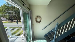 A balcony with a white chair, a glass door, a blue staircase, and a decorative wreath on the wall. - Shipwreck Villa (Chincoteague)