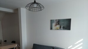 A modern living room with a grey sofa, a wooden coffee table, a dining area with a wooden table and chairs, and a ceiling light fixture. - Charming Mersoise house 7 minutes walk from the beach with private covered parking (Mers-les-Bains)