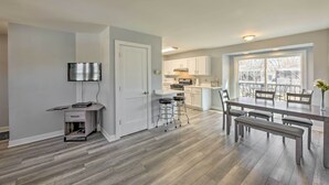 Una cocina moderna con armarios blancos, una zona de comedor con mesa y bancos de madera, y un ventanal con vistas al exterior.