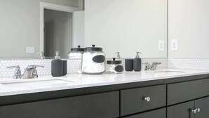 Een moderne badkamer met twee wasbakken, een grote spiegel en opbergpotten op het aanrecht.