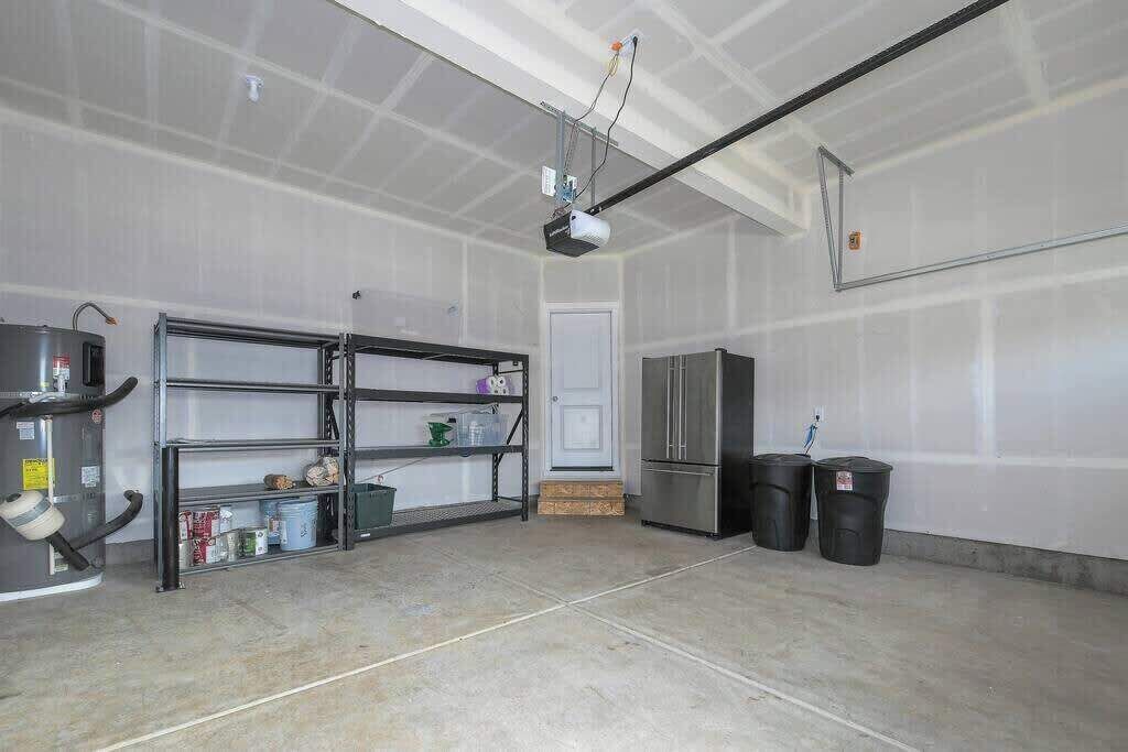 Een garage met een aan het plafond bevestigde projector, een koelkast en planken met diverse spullen.