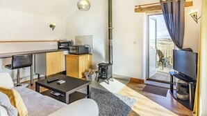 Ein kompakter Wohnbereich mit Küchenzeile, einer Couch, einem Couchtisch, einem Fernseher und einem Balkon mit Blick.