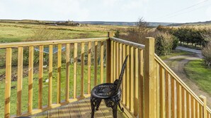 Eine Holzterrasse mit einem Metallstuhl, mit Blick auf eine ländliche Landschaft mit Feldern und einem entfernten Gebäude.