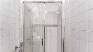 Cabina de dutxa tancada amb vidre, rajoles blanques, vàter de mà i porta de vidre.