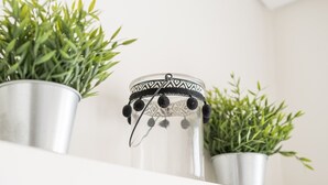 Un recipient metàl·lic amb tapa estampada i detalls negres, col·locat sobre una balda blanca amb dues plantes en testos.