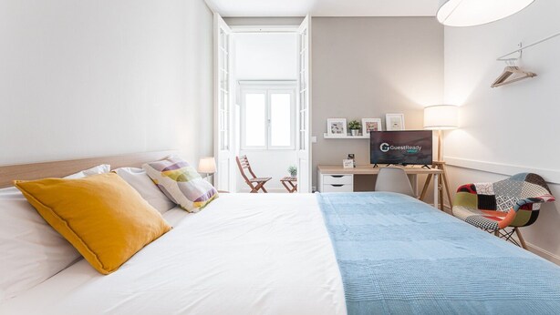 Una habitació d'hotel amb un llit, un escriptori, una cadira, un televisor i una làmpada.