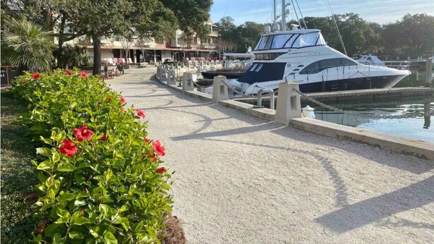 En småbåtshamn med en vit lyxyacht förtöjd, omgiven av grönska och med en byggnad i bakgrunden.