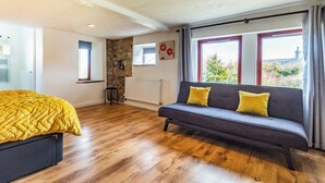 Un dormitorio con cama, sofá, pared de piedra, ventana y radiador.