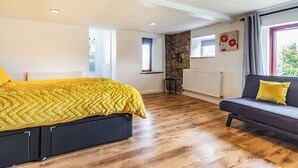 Un dormitorio con cama, sofá, pared de piedra, radiador y ventana con cortinas.