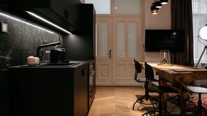A modern kitchen with a black countertop, a coffee machine, and a wooden dining table with chairs. - TG Hotel Apartments Budapest (Budapest)