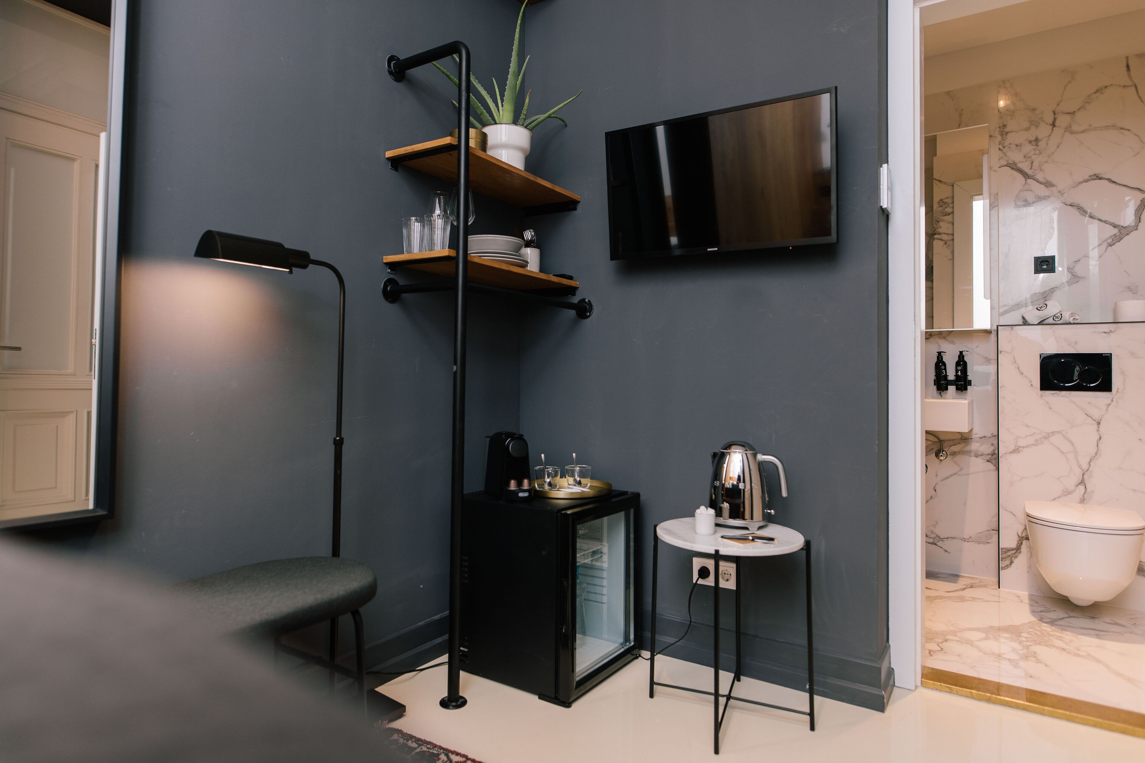 Un baño moderno con pared de mármol, televisor montado, un pequeño rincón de café y un diseño minimalista.