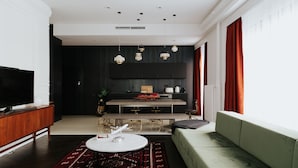 A modern living room with a sofa, a coffee table, and a TV. There is a kitchen area with a dining table and chairs. - TG Hotel Apartments Budapest (Budapest)
