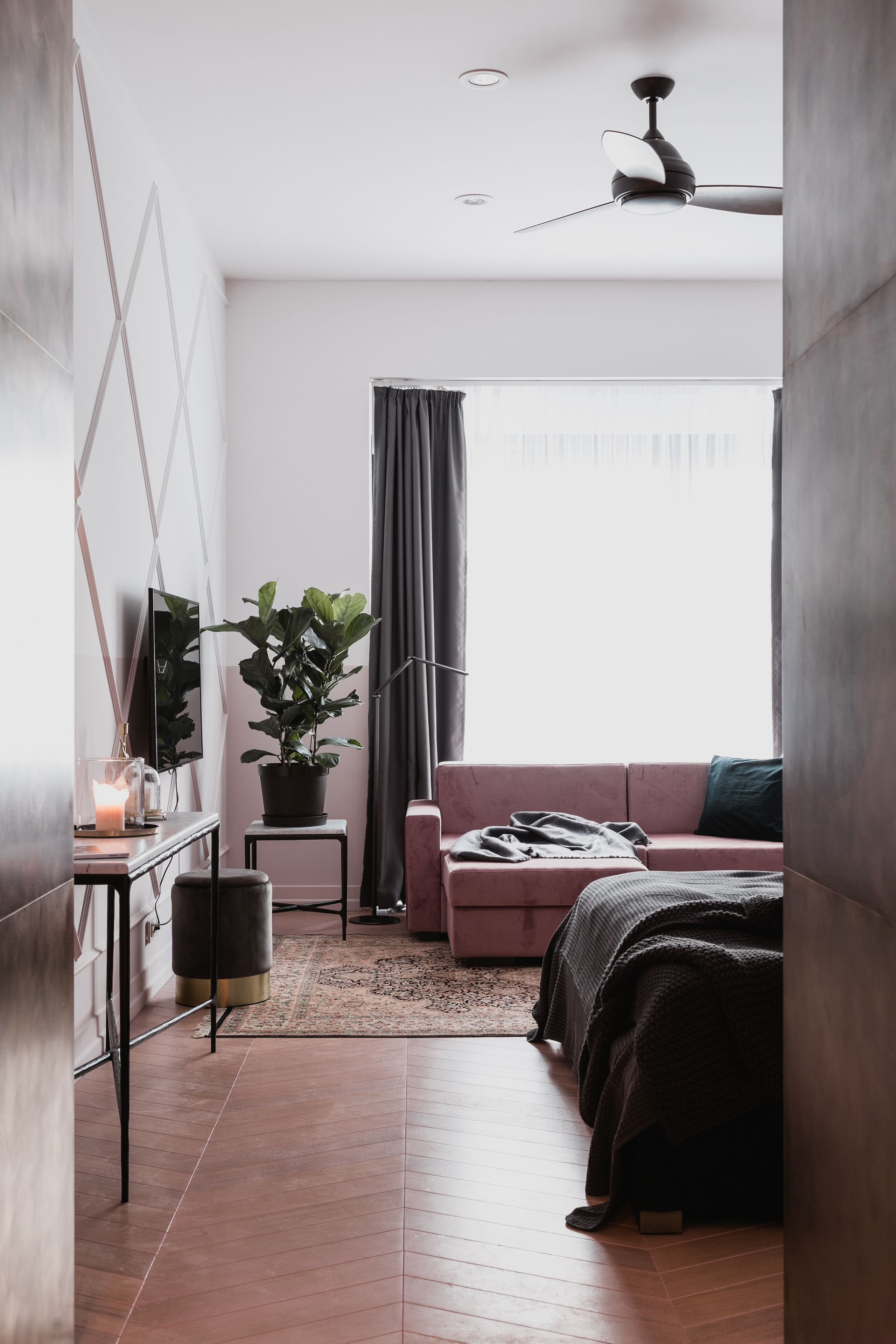 Un dormitorio moderno con cama, escritorio, planta en maceta y un amplio ventanal con cortinas.