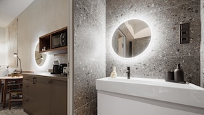 A modern bathroom with a granite countertop, a round mirror, and a built-in sink. - TG Hotel Apartments Budapest (Budapest)