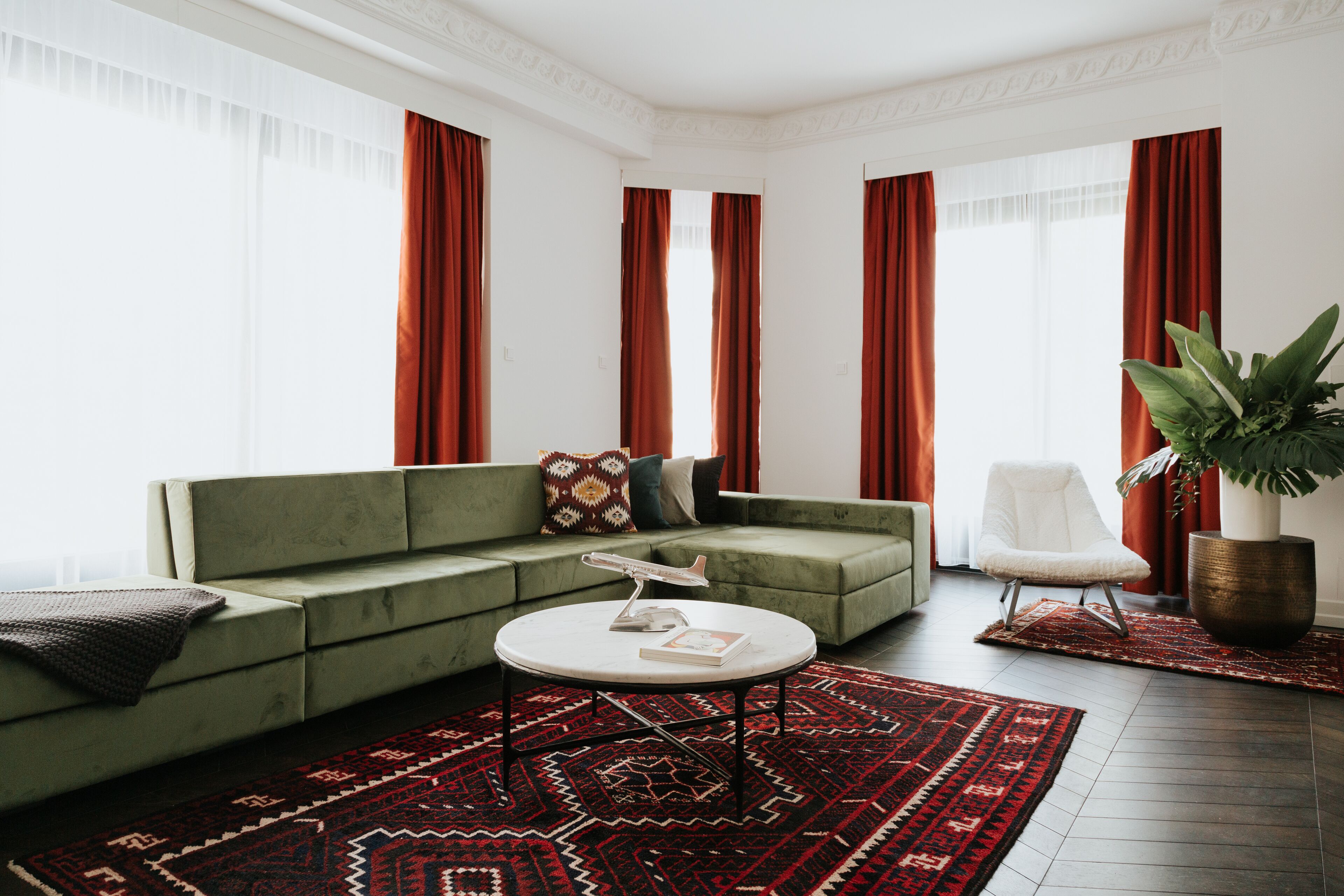 A modern living room with a green sofa, a white armchair, a round coffee table, and a large potted plant.