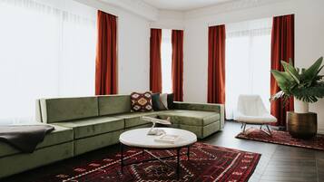 A modern living room with a green sofa, a white armchair, a round coffee table, and a large potted plant.