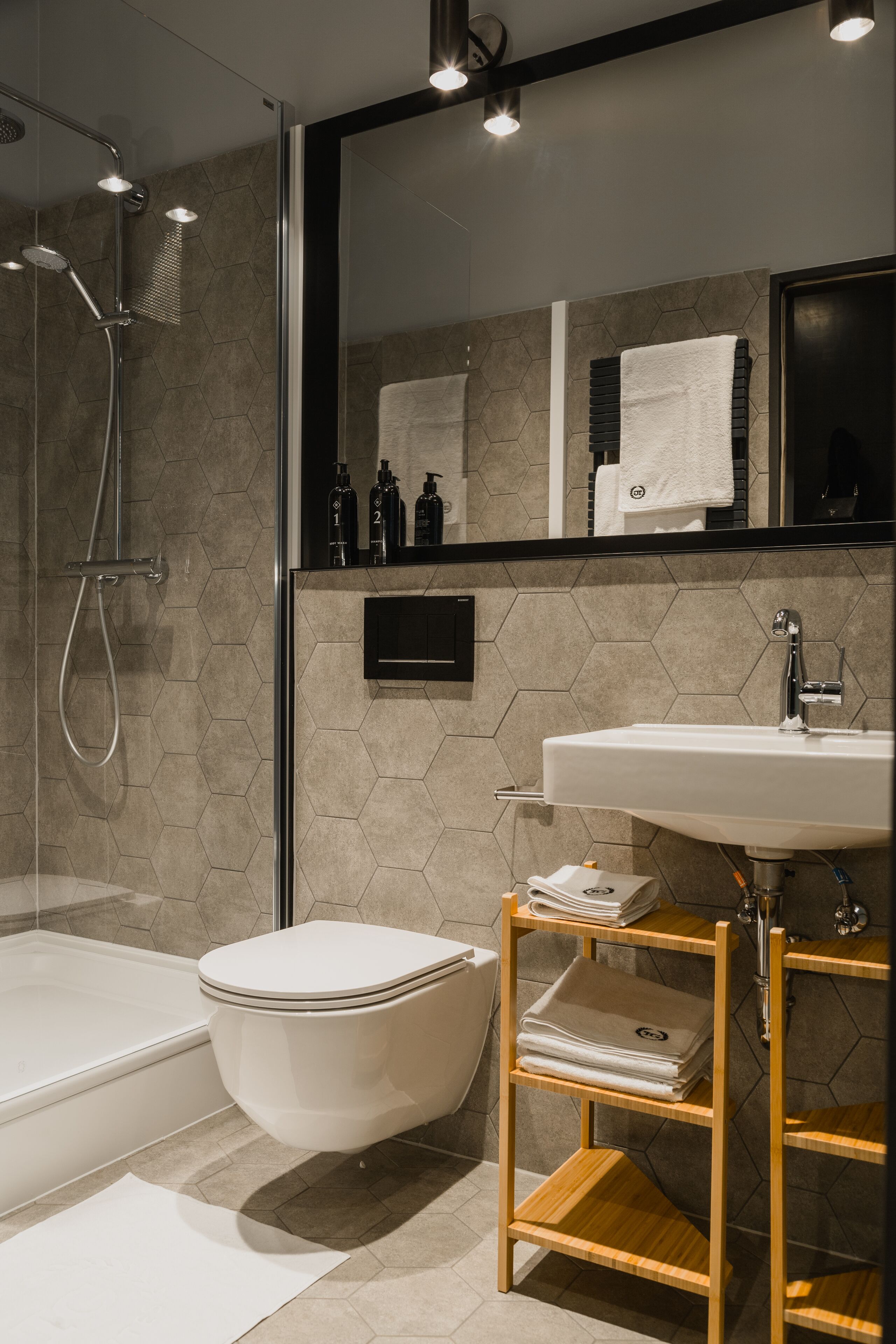 A modern bathroom with a glass-enclosed shower, a white bathtub, a toilet, and a wooden vanity with a sink.