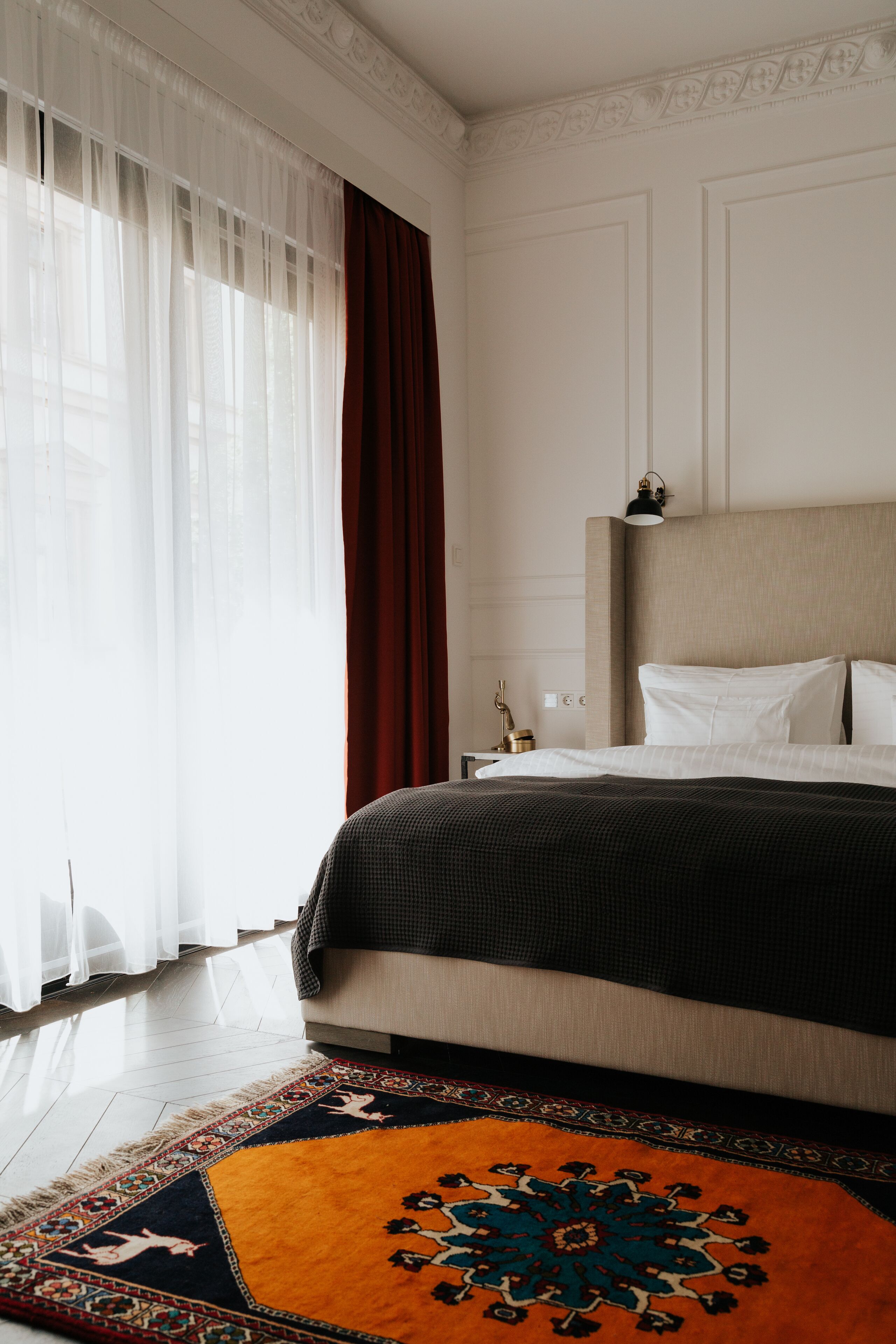 A hotel room with a bed, a nightstand, a lamp, and a patterned rug.