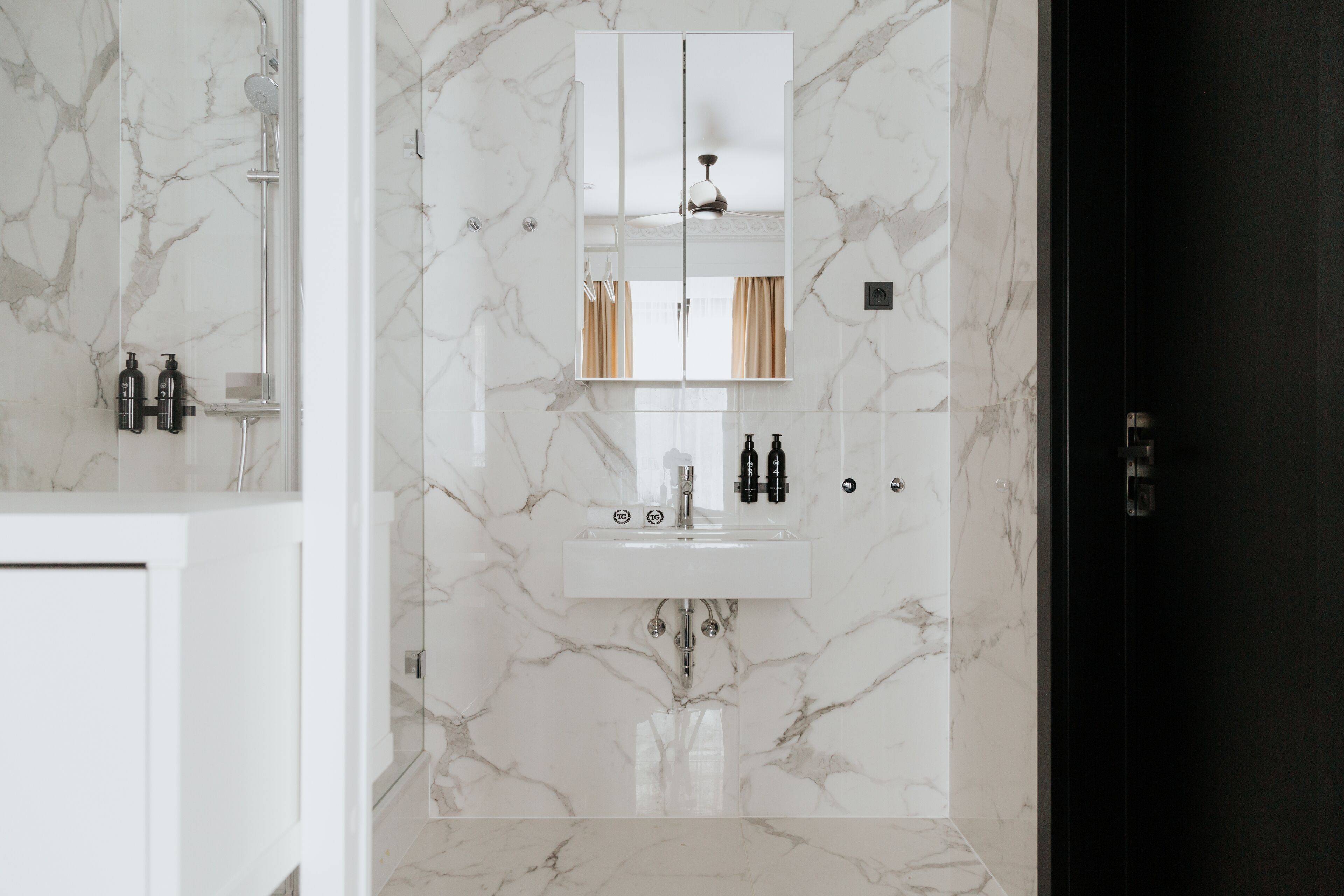 A bathroom with a marble floor, a white sink with two faucets, and a mirror above the sink.