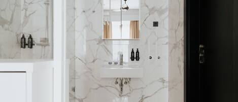 A bathroom with a marble floor, a white sink with two faucets, and a mirror above the sink.