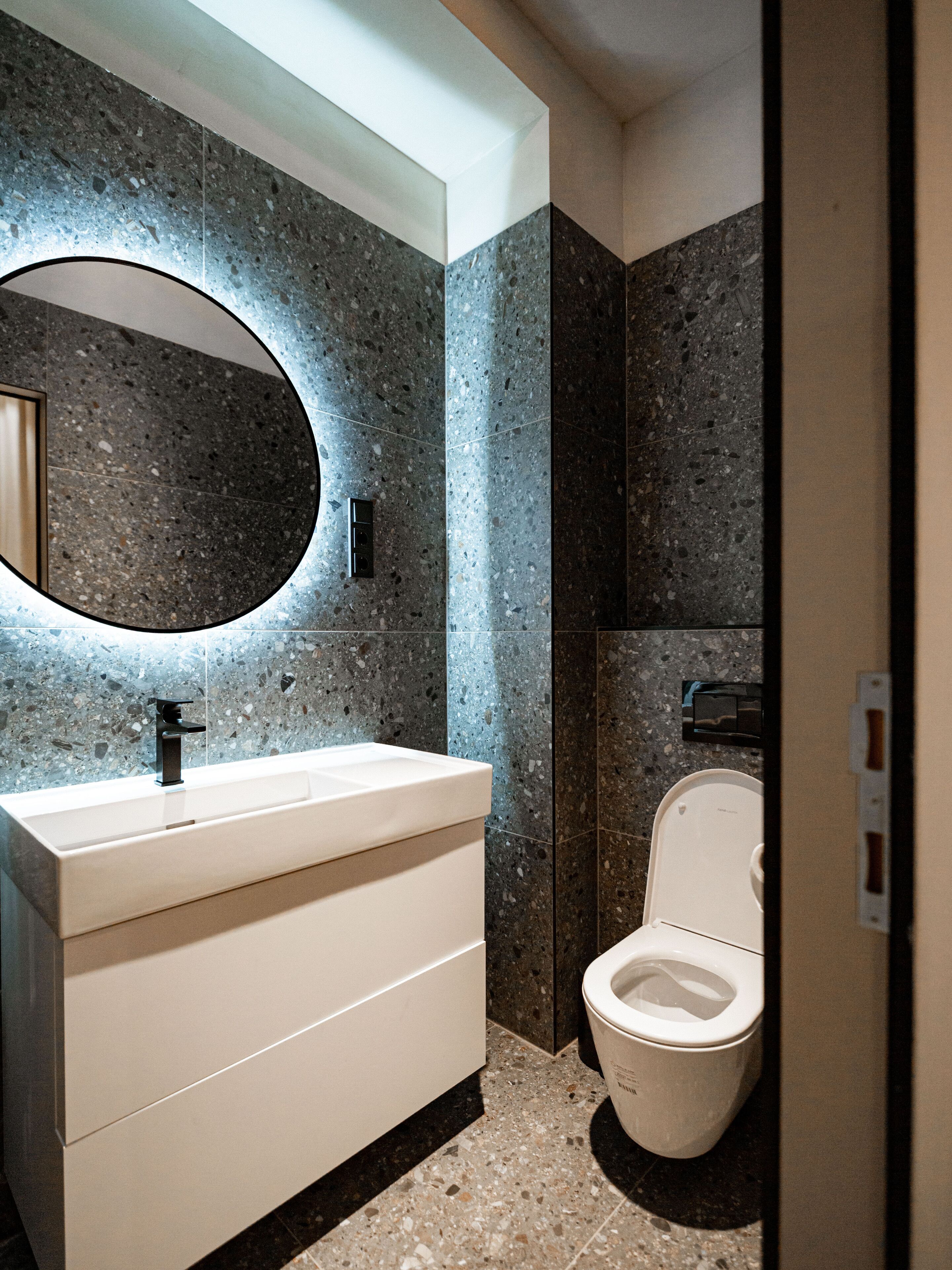 A modern bathroom with a granite countertop, a large oval mirror, and a toilet.
