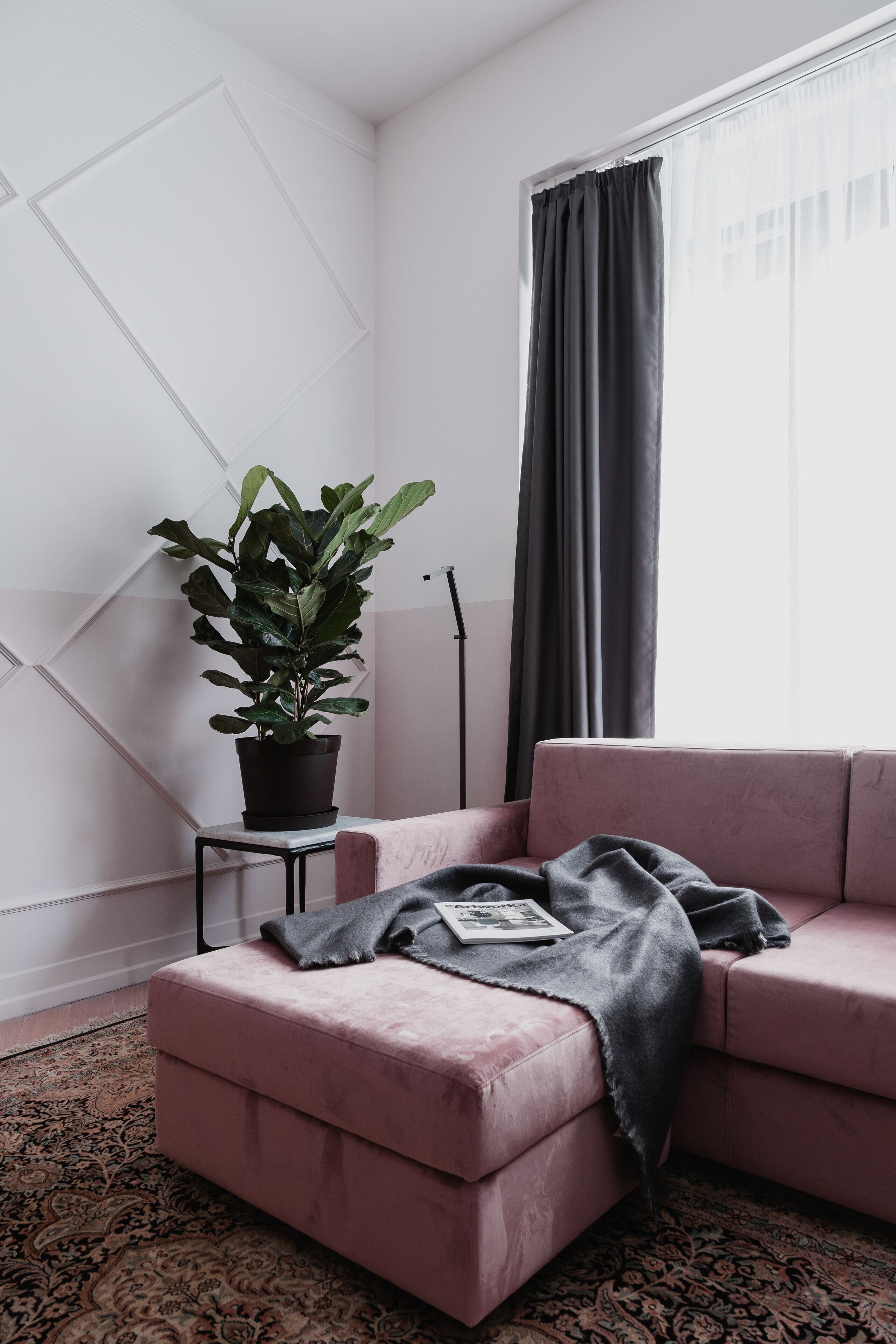 Un salon moderne avec un canapé rose, une petite table sur laquelle est posée une plante en pot et un tapis à motifs.