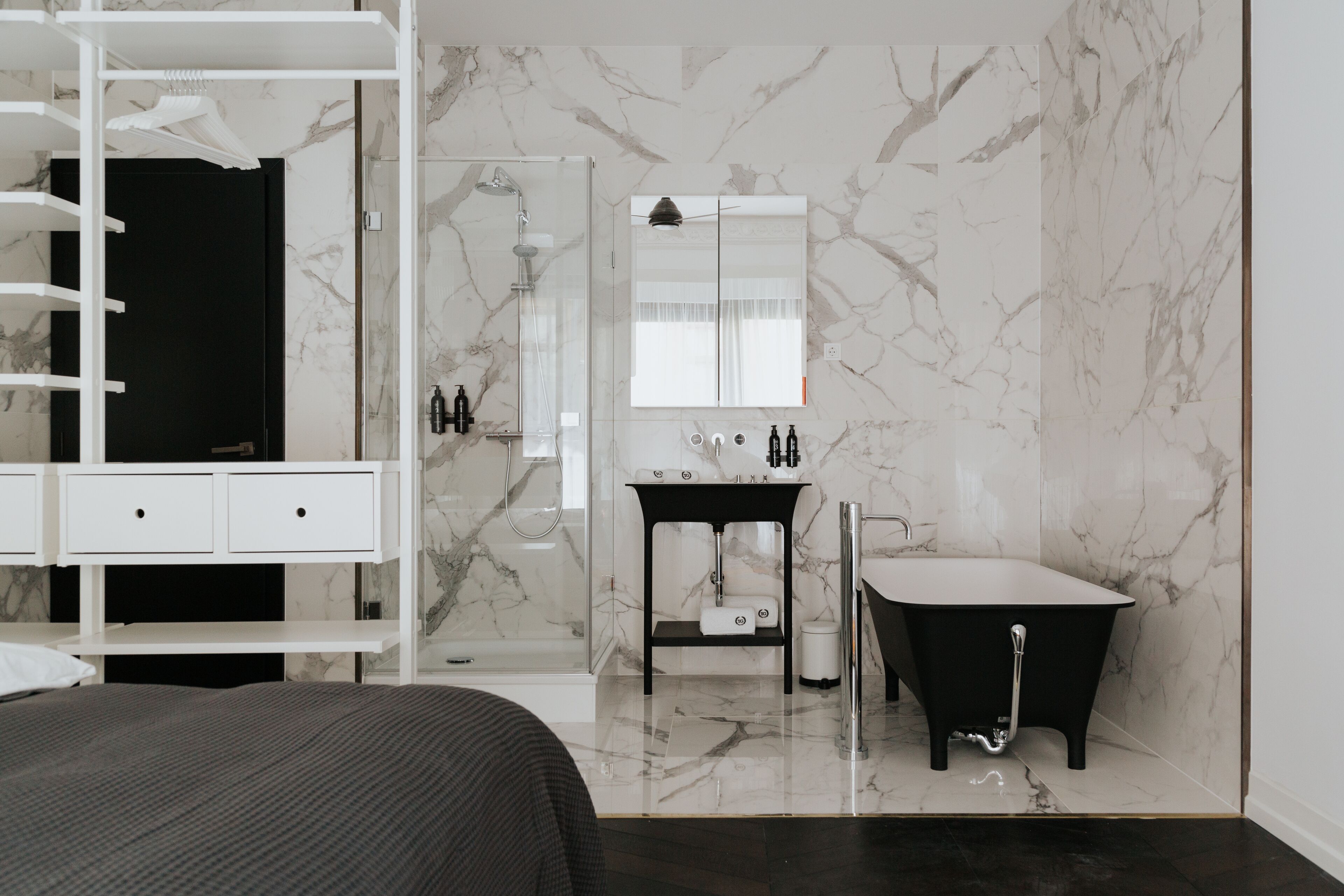 A modern bathroom with a glass shower enclosure, a black freestanding bathtub, and a vanity with a mirror.